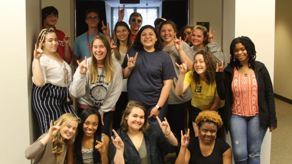 call center student workers standing together holding up the wolf hand sign