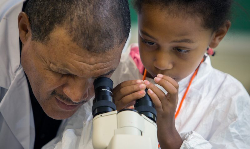 Tracy Hanner peering through a microscope alongside a young Black student