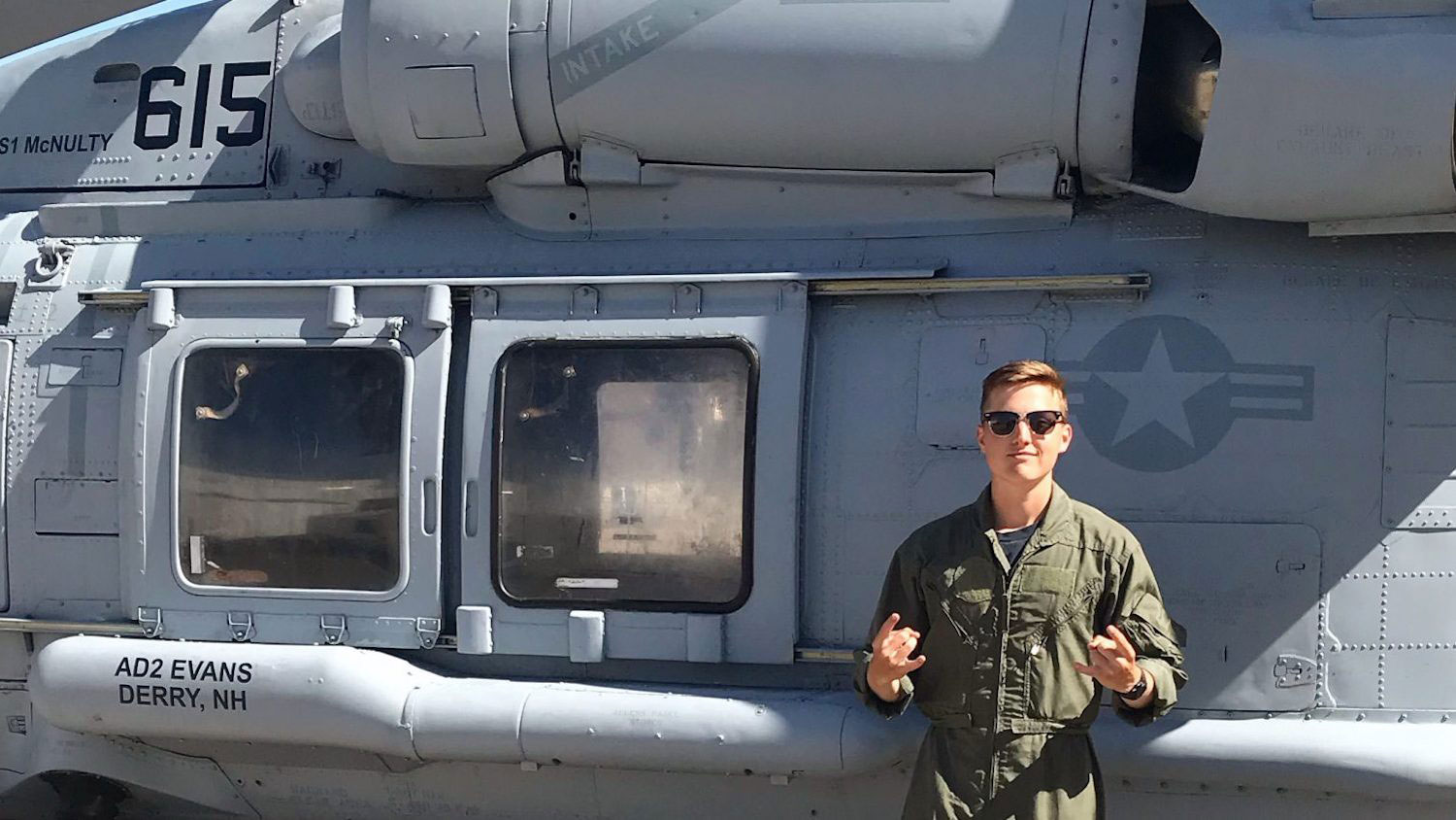 Garrett Welsh doing the wolf hands in front of a military helicopter