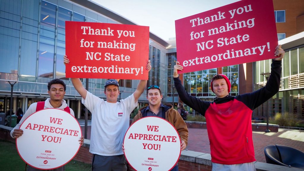 four young male students holding signs that say We Appreciate You and Thank You For Making NC State Extraordinary