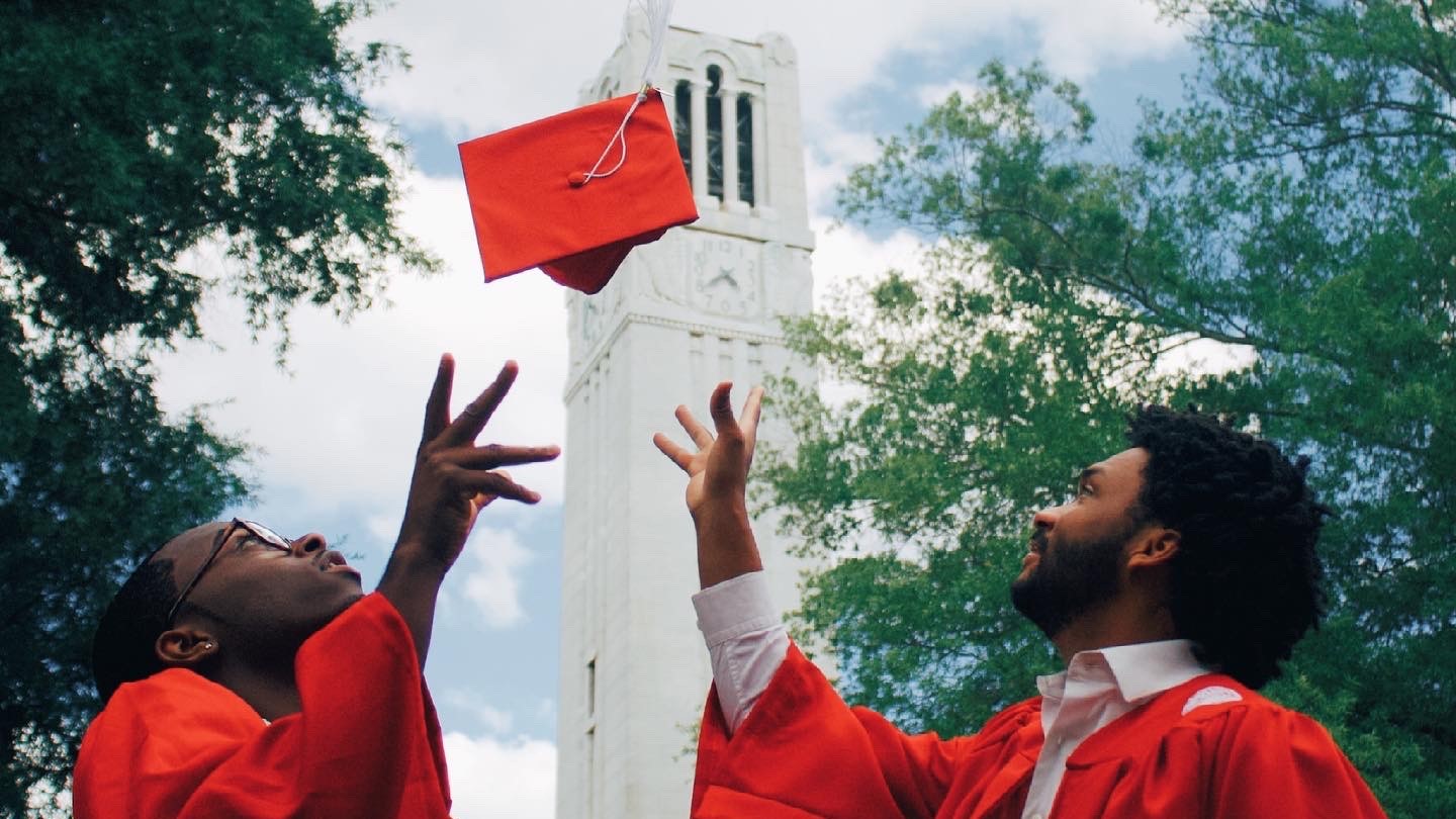 Image of Graduates Eisley Parks Davion Anderton throwing hats up by tower for a photo Contest
