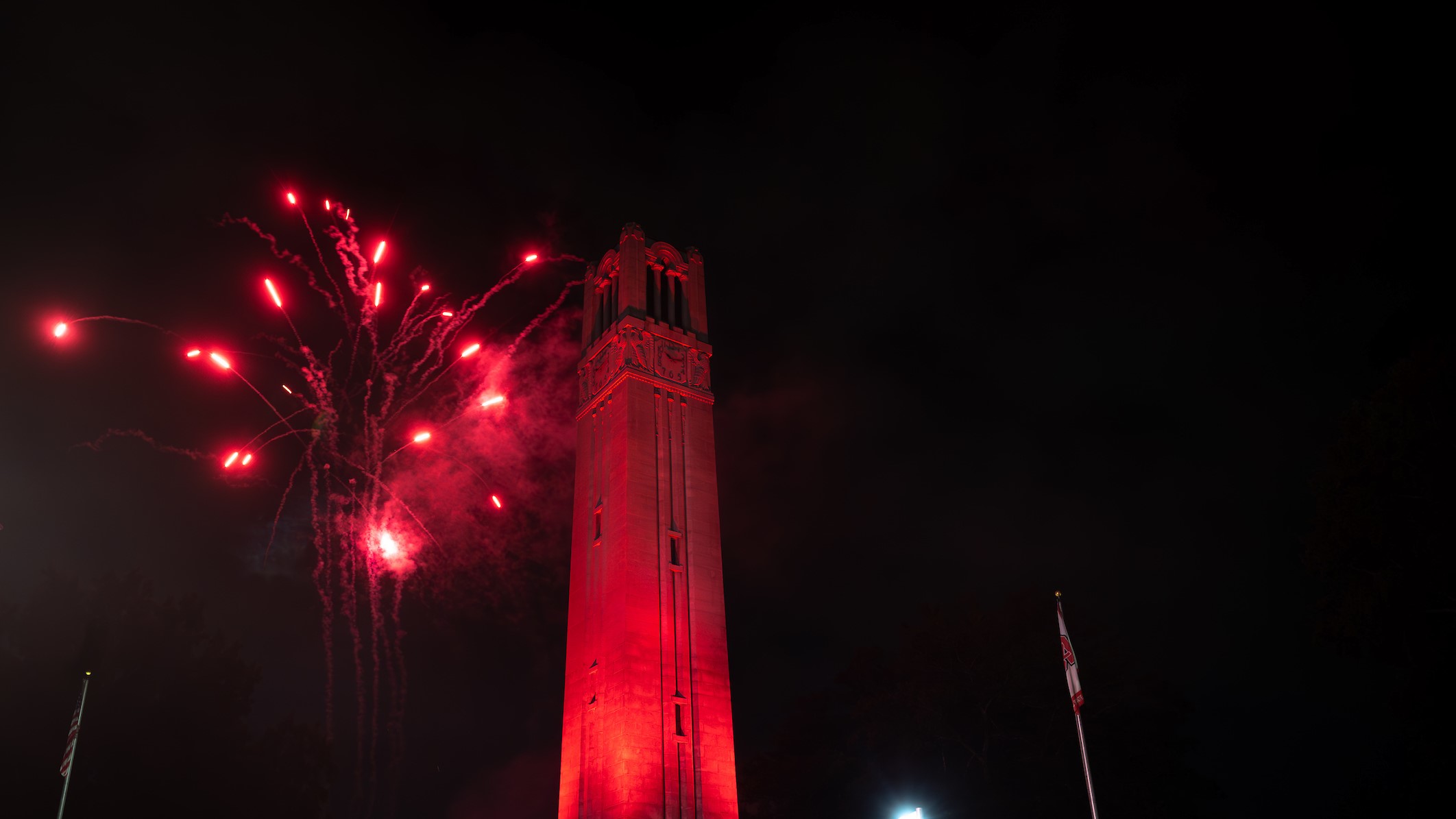 the belltower lit red with fireworks bursting above it