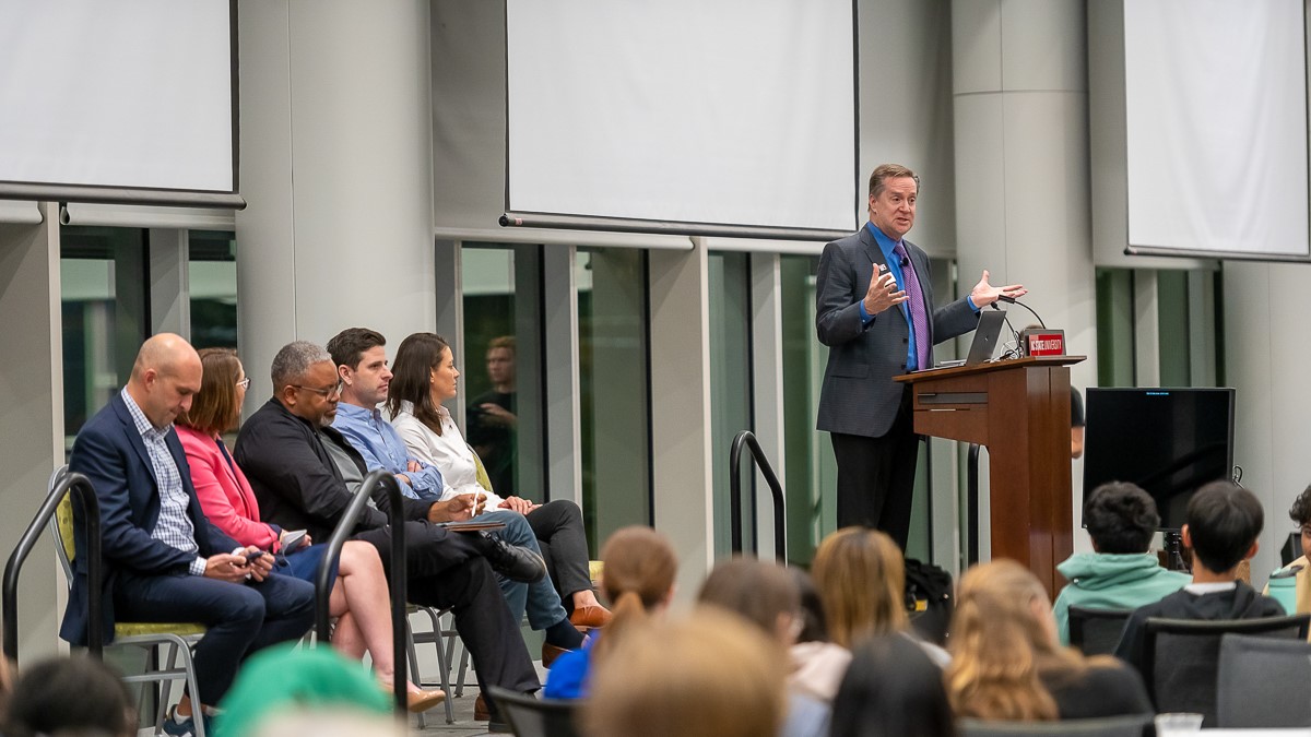 Chuck Flink, far right, addresses event attendees on a stage with fellow panelists to his left